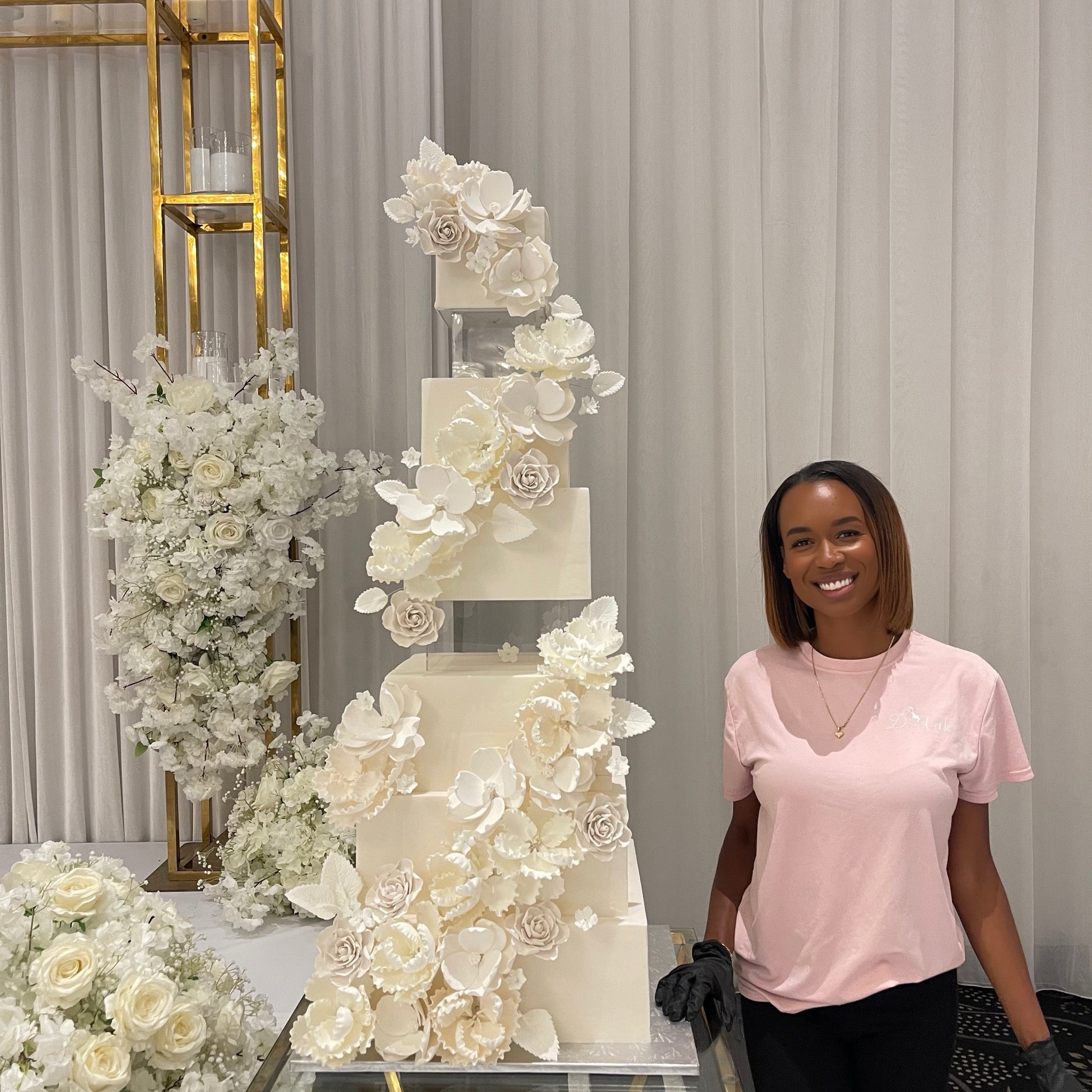 Stéphanie Dédé souriante à côté d'un grand gâteau de mariage à fleurs en sucre blanches, Dcake